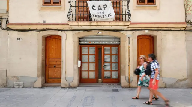 Una pareja pasa frente a una residencia con una aviso que lee en catalán: "No hay pisos turísticos" 