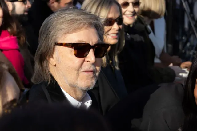 Paul McCartney sentando en un evento con lentes oscuros