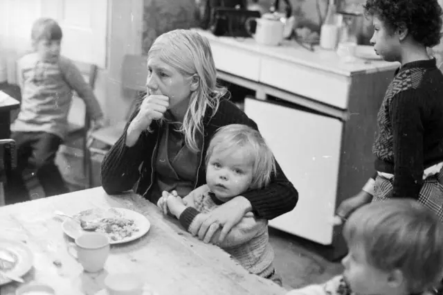 Mujer sentada a la mesa con niño y comida, y más niños alrededor