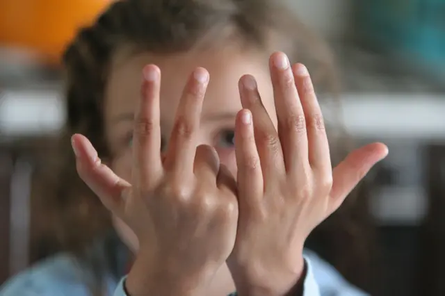 Una niña mostrando 8 dedos delante de su cara. 