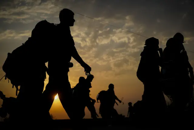 Un grupo de personas con equipaje a la espalda, caminando antes del atardecer.