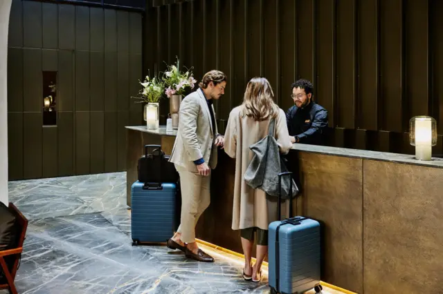 Una pareja con equipaje frente a la recepción de un hotel