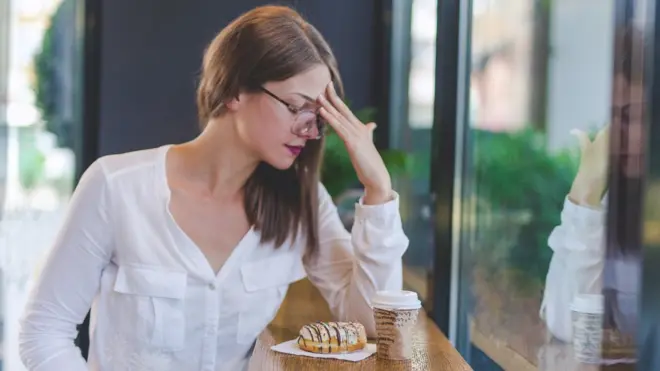 Mujer que no se encuentra bien frente a café y dulce.