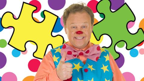 Mr Tumble is smiling with a thumbs up, with jigsaw pieces surrounding him.