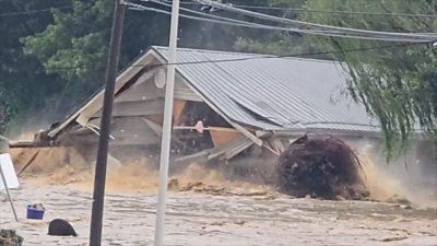 The roof of a house is seen in front of a wave of muddy water