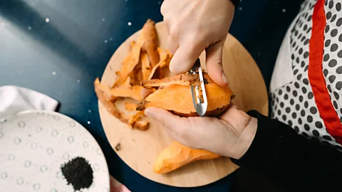 A person peels a sweet potato using a peeler (Credit: Getty Images)