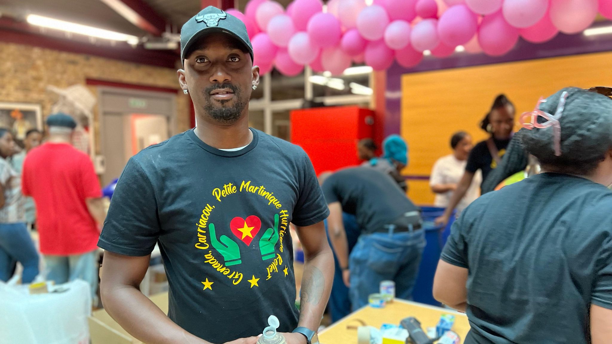 Esmond Joseph stands in a community hall with volunteers in the background