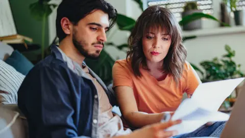 A man and woman sitting in a front room and looking anxiously at bills 