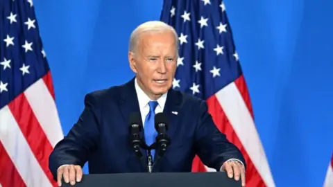 Joe Biden standing in front of American flags