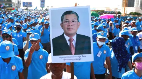 EPA A crowd of ruling party supporters wearing blue uniforms and hats march in Phnom Penh on 1/7 in support of Hun Sen, with one carrying a large placard bearing the PM's picture