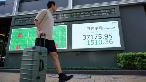 A man walks in front of an electronic quotation board displaying share prices on the Tokyo Stock Exchange.