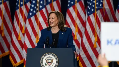 Kamala Harris standing at podium with American flags behind her