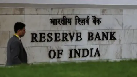 Signage at the Reserve Bank of India (RBI) headquarters building in Mumbai, with a man wearing a jacket and yellow shirt walking in the forefront. 