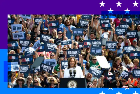 Kamala Harris on stage at a rally with supporters photographed in the background 