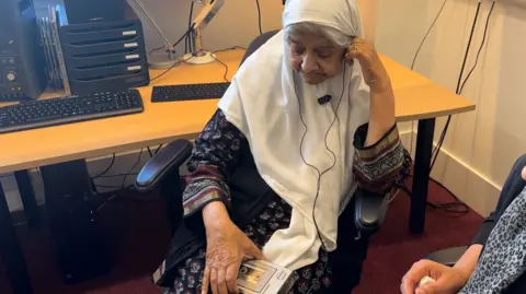 Woman sat in front of a desk listening to a portable cassette recorder