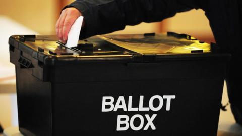 Black ballot box with someone posting a vote through the slot.