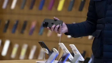 A hand holds a black iPhone in an iPhone store