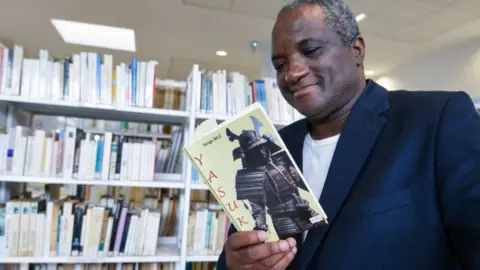 Getty Images French-Ivorian writer Serge Bile reads a copy of his last book "Yasuke" at the library of the French Cultural Centre (CCF) in Abidjan on 28 March 2018.