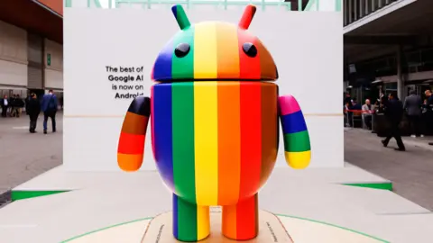 Google Android logo and mascot displayed as a statue with the rainbow LGBTQ+ pride flag colors on Google's Android Avenue at the Mobile World Congress 2024 in Barcelona, Spain, on March 25, 2024. 