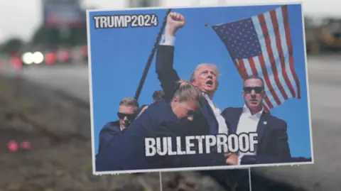 A roadside poster saying 'BULLETPROOF' with a picture of Trump raising his fist after the shooting