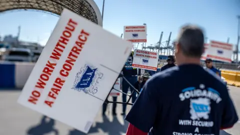 Dockworkers attend a demonstration and hold signs up at the Port of Miami on the first day of the East and Gulf Coast cargo facilities dockworkers strike in Miami, Florida, USA, 01 October 2024. 