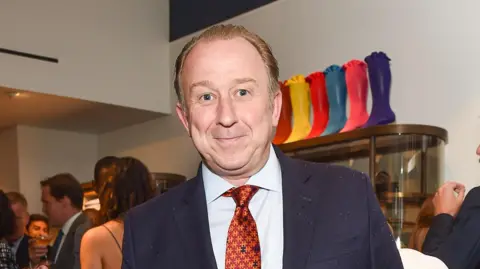 Nigel Blow wearing a suit and patterned red and orange tie at the opening of the Turnbull and Asser store in Mayfair, 2015