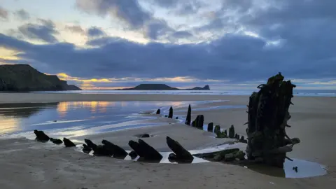 Rhossili beach you can also see the remains of the Helvetia, shipwrecked in 1887 on the sands and visible during low tide, twilight, reflections of the setting sun is visible in the wet sand.