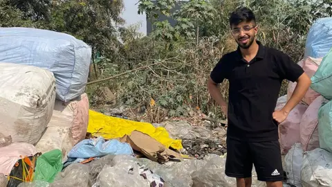 Vivek stands beside litter piled high in large sacks 