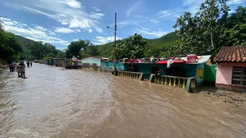Getty Images  People stand outside their flooded homes after a river swelled due to heavy rains following the passage of Hurricane Beryl on the road from Cumana to Cumanacoa, Sucre State, Venezuela, on July 2, 2024