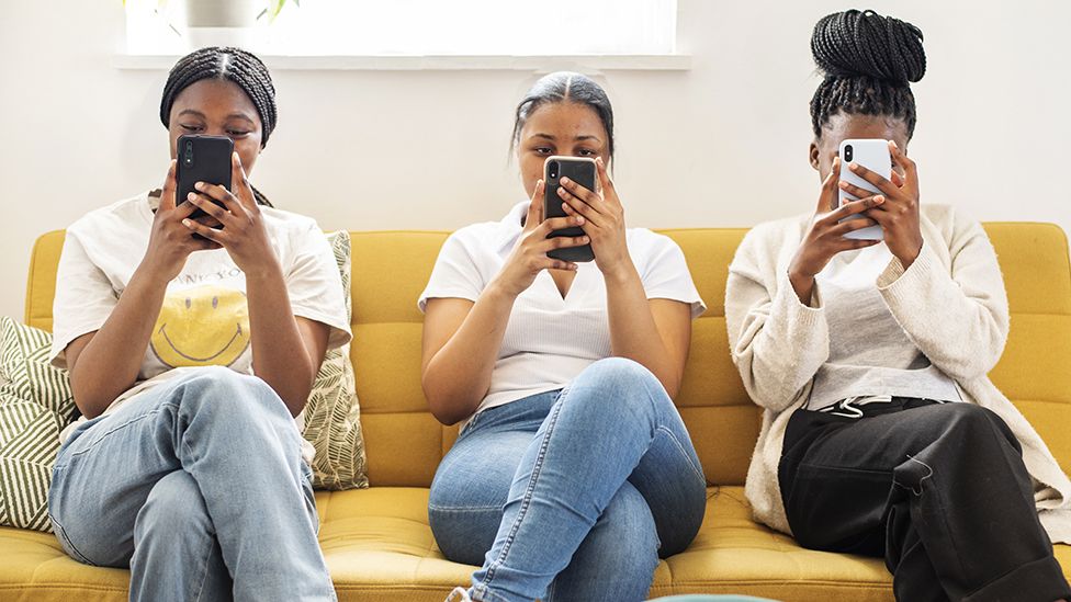 Three people using smartphones on a sofa