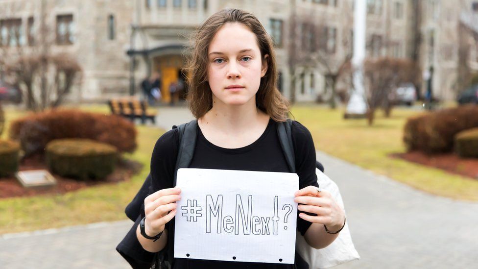 Violet Massie holding up a sign reading 'Me Next?'