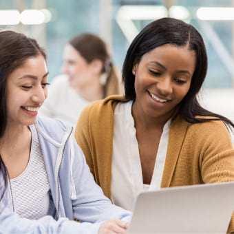 A teacher sitting by a student looking at a laptop.