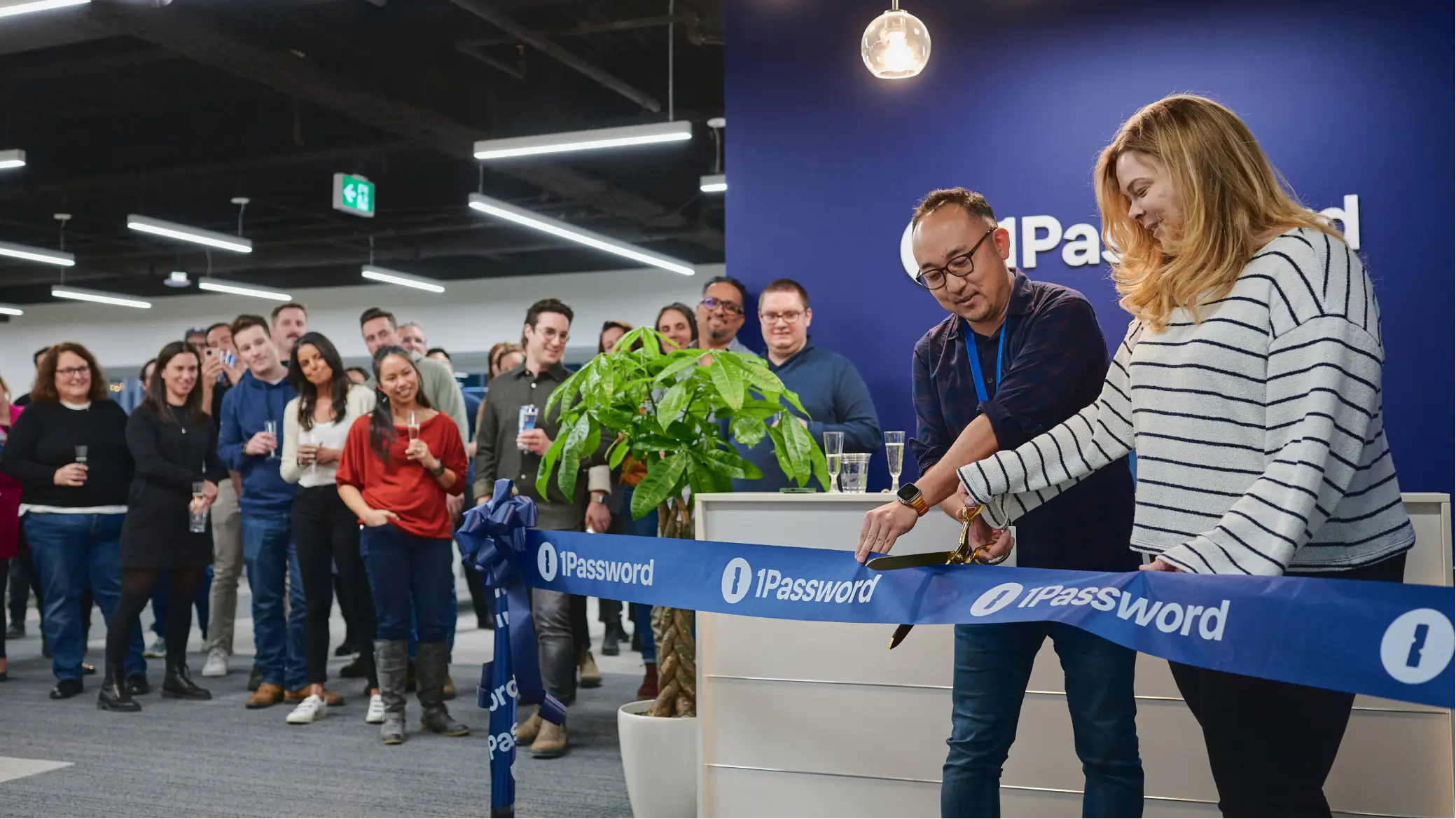 Ribbon-cutting ceremony in the 1Password office with people gathered and a blue "1Password" ribbon.