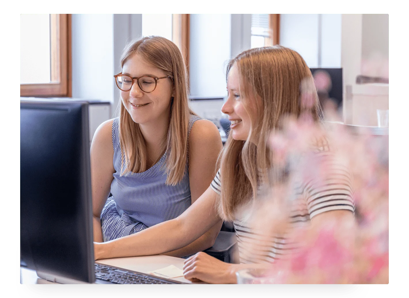 Photo of two young girls smiling and sitting in front of a computer at Trustpilot's office