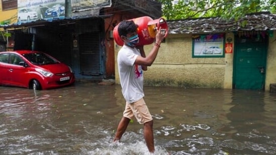 A man carries a cooking gas cylinder and wades past a waterlogged street in Chennai as the city witnesses torrential showers for the second time in five days.(AP)