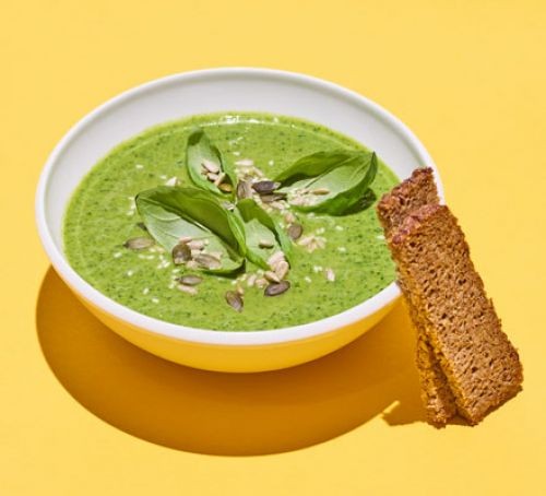 Bowl of courgette soup topped with basil leaves, with crackers