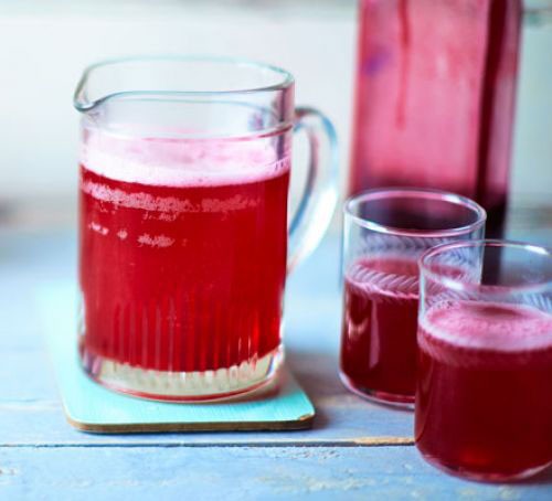A jug of blackcurrant cordial with glasses on a table