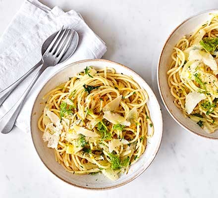 Two bowls of fennel spaghetti on a white table with cutlery alongside
