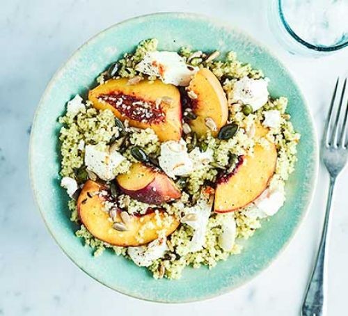 Bowl of couscous topped with sliced peaches and feta