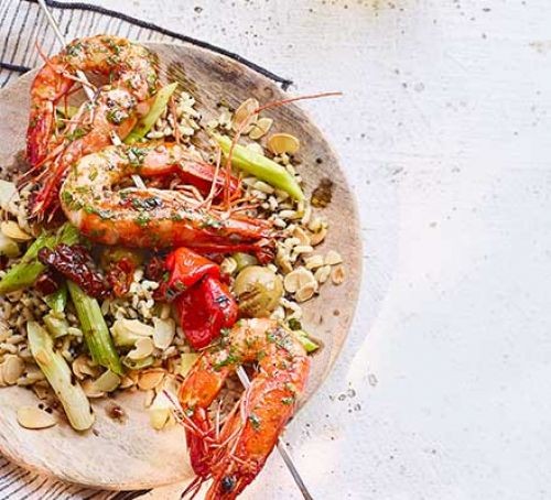 Barbecued prawn and pepper skewers on a plate with rice and salad