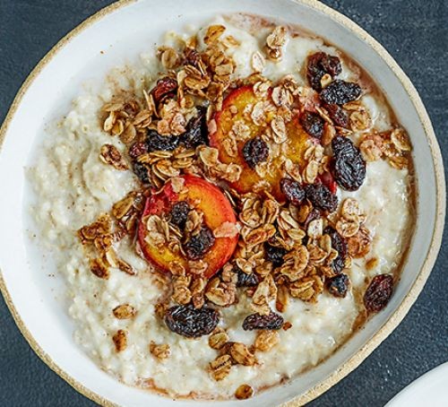 Bowl of porridge topped with plum, raisin and granola topping