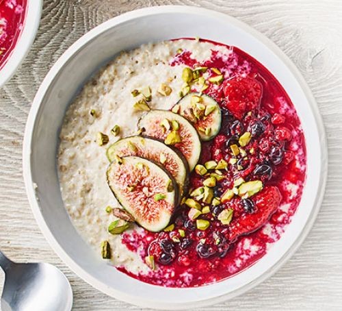 Bowl of porridge with berry compote, topped with sliced figs and chopped nuts