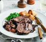 Beef brisket on a plate with roast potatoes and vegetables alongside knife and fork