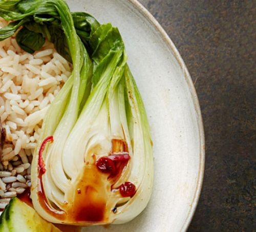 A bowl of steamed pak choi, sliced in half, on a bed of rice