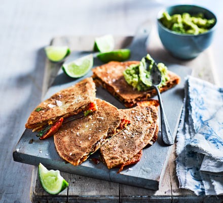 Stack of quesadillas on a slate with lime and guacamole