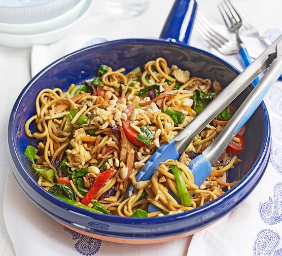 Vegetable stir-fry with crunchy peanuts served in a blue cast iron pan with tongs for serving