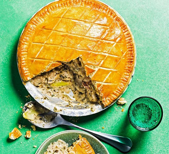 Wild garlic, chicken & leek pie with a serving spoon against a green backdrop