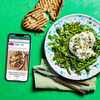 A phone with the Good Food app on its screen plus a green salad topped with burrata