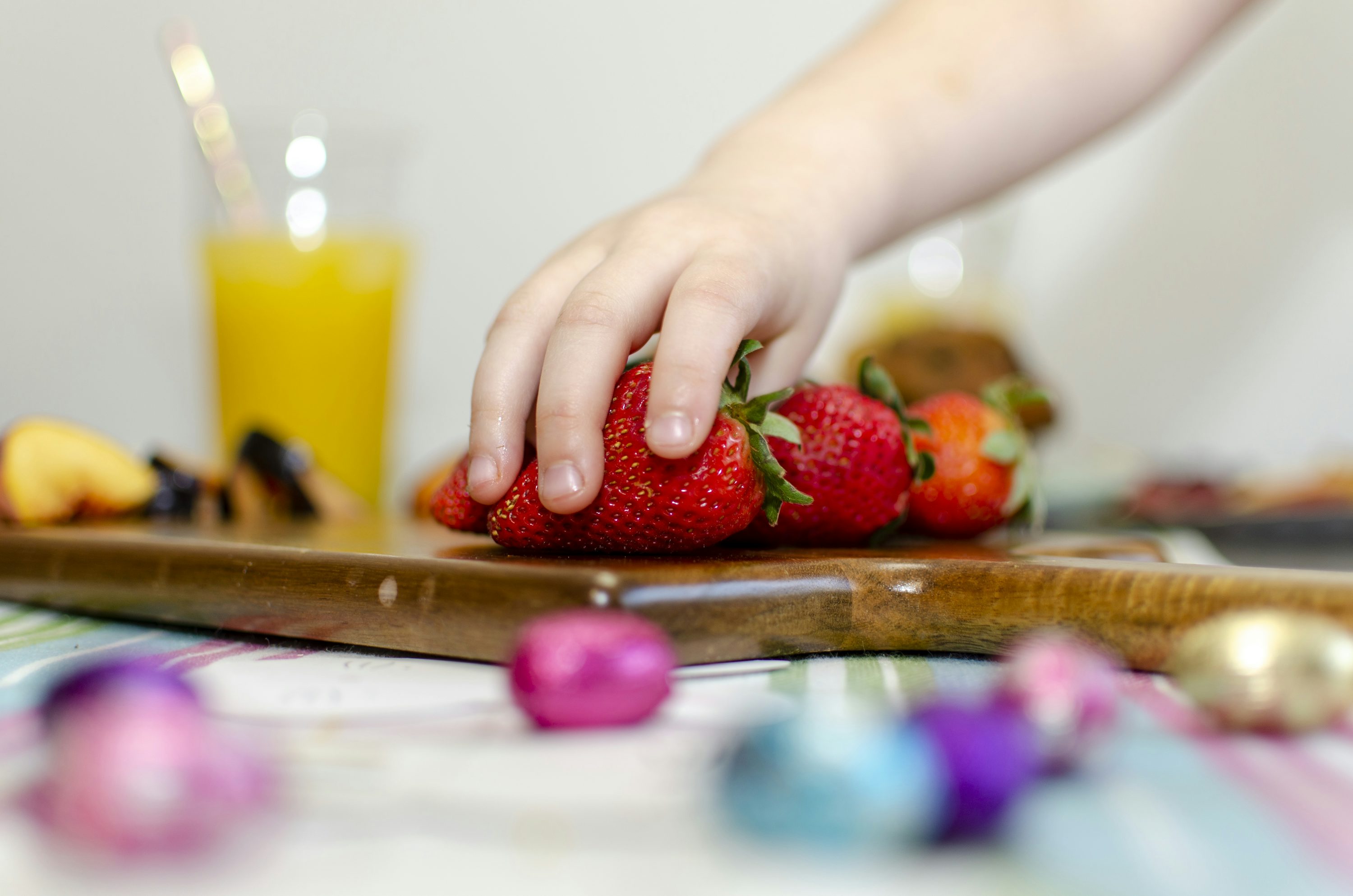 person holding strawberries on brown wooden chopping board
