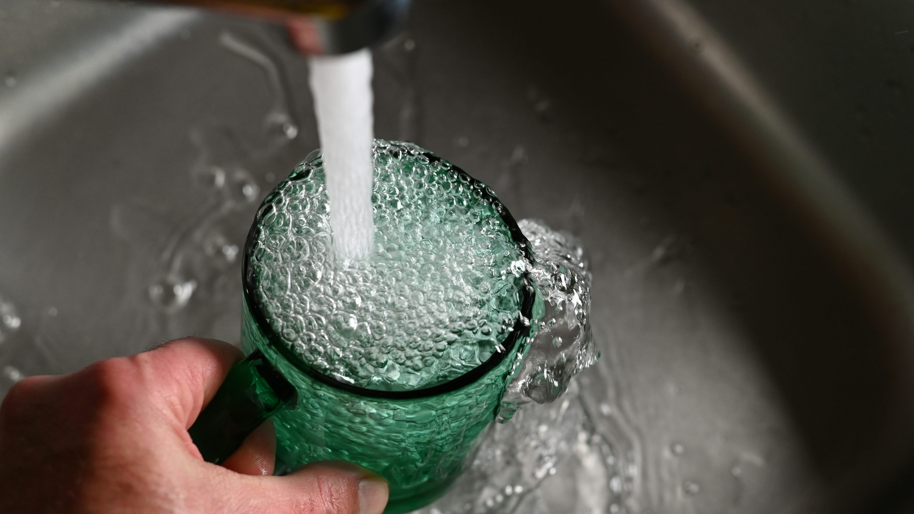 Die Hand einer Person hält einen grünen Becher, aus dem Wasser herauskommt